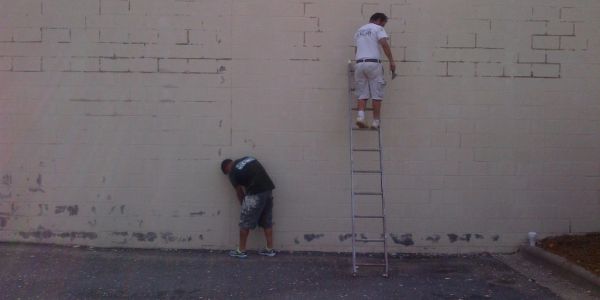 Two men working on a wall, one on a ladder.