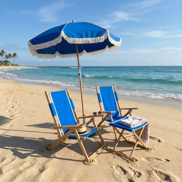 Two blue beach chairs and an umbrella on a sandy shore by the ocean.