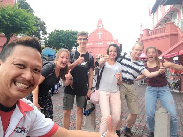 Tour group happily posing with thumbs up in front of Christ Church Melaka.