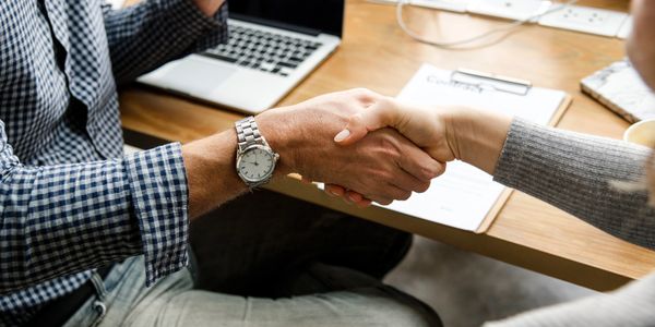 Two people shaking hands across a desk in a professional setting.