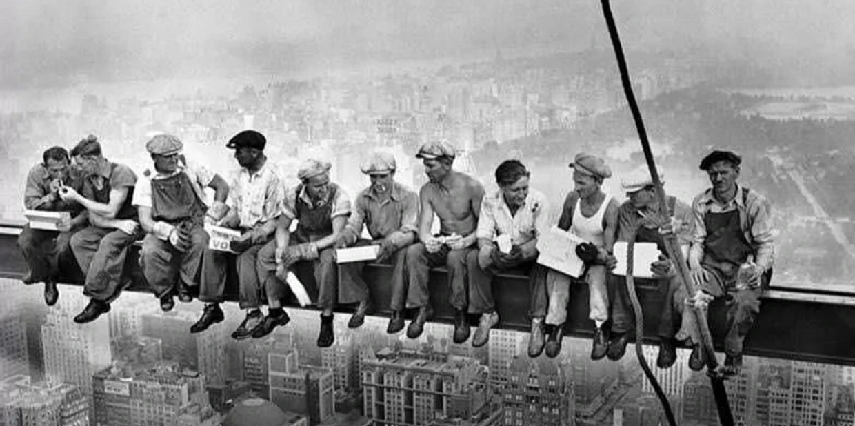 Group of guys sitting on an I-beam over a city scape from the early part of the century. 