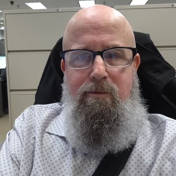 Man with a bald head, gray beard, and glasses sitting in an office.