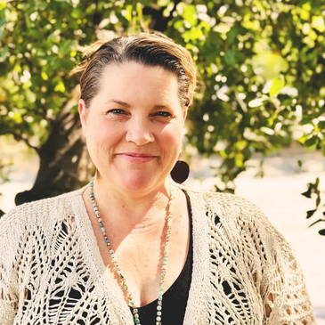 Smiling woman wearing a knitted cardigan and beaded necklace outdoors.