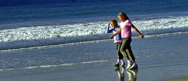Two children walk happily along a sunny beach, with gentle waves in the background