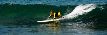 A child in a black and yellow wetsuit relax surfboard on a sandy beach 
