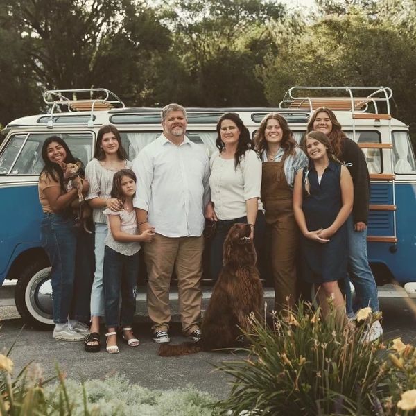 A family with their dogs posing in front of a blue VW Bus for a family portrait.