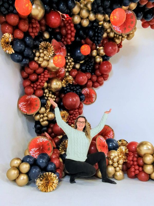 Girl sitting in front of a Chinese new year themed balloon wall with arms up in the air