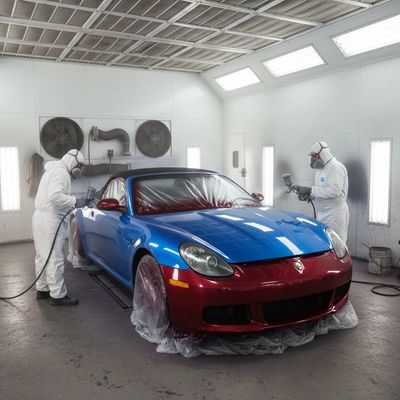 Two workers in protective suits painting a red and blue sports car in a spray booth.