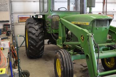 Green John Deere tractor inside a garage or workshop.