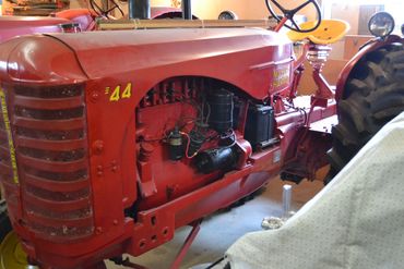 Close-up of a vintage red tractor with visible engine parts indoors.