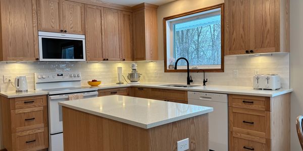 Modern kitchen with wooden cabinets and white countertops under soft lighting.