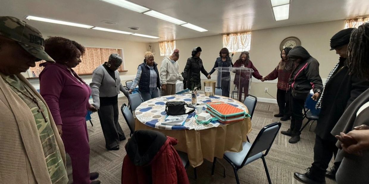 Group of people holding hands in a circle around a table in a room.
