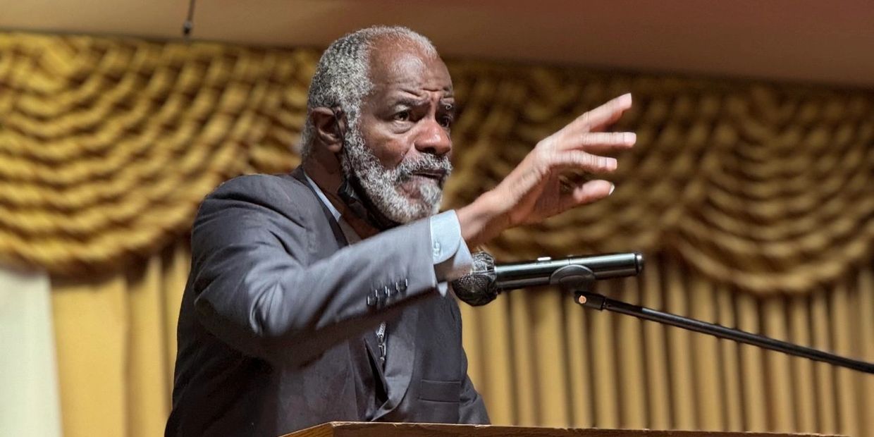 Elderly man in a suit passionately speaking at a podium with a microphone.