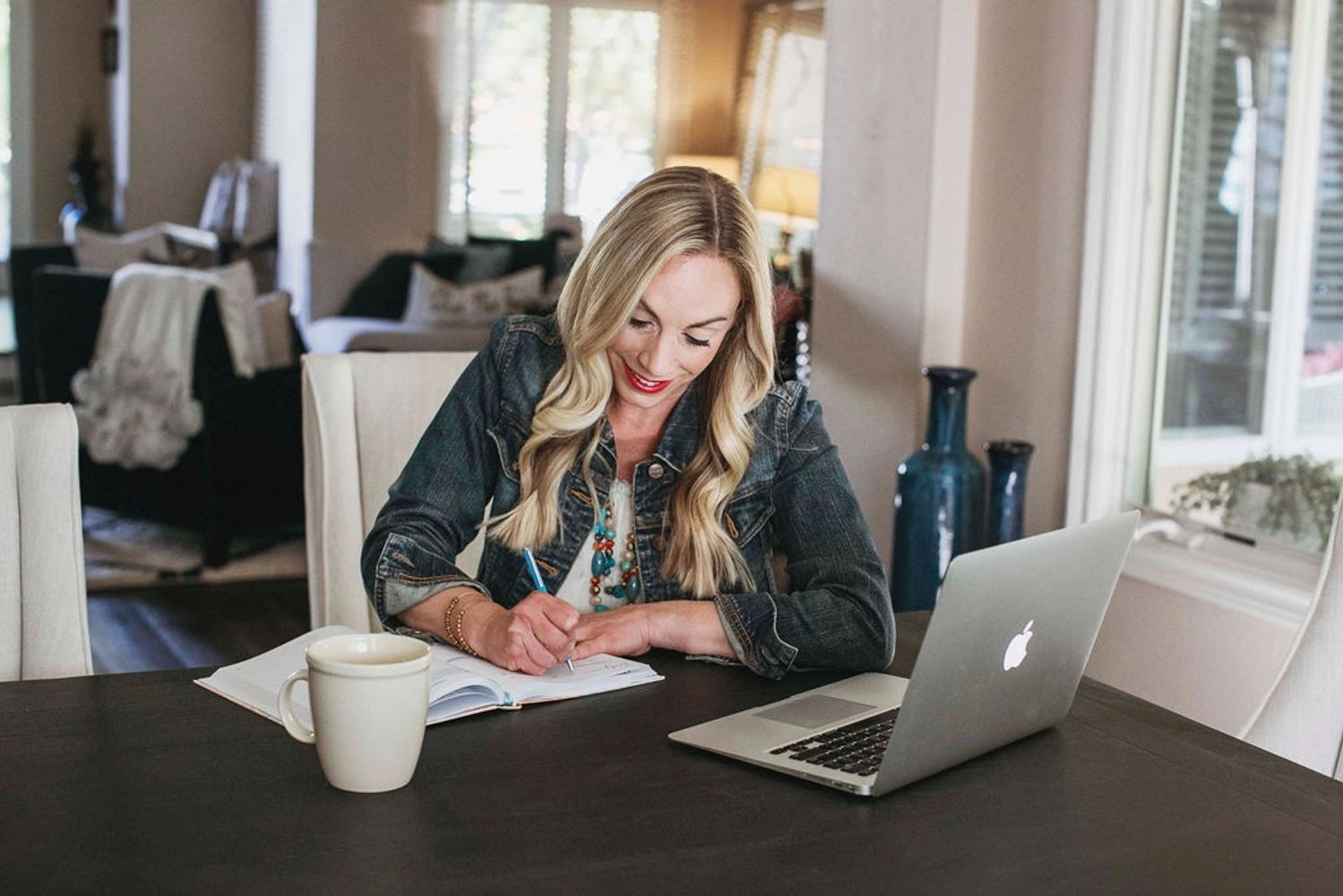 Business coaching writing in a notebook at a table with a laptop and coffee cup.