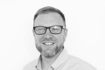 Smiling man with glasses in a black and white portrait.
