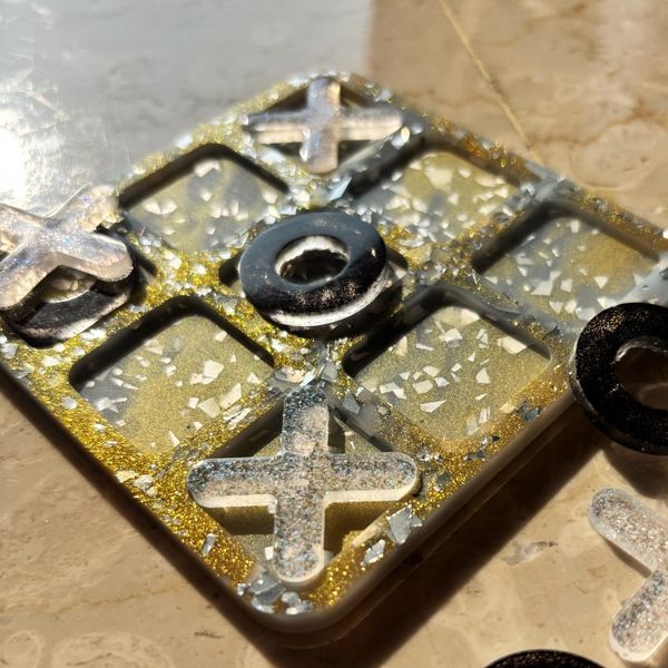 Close-up of a glittery tic-tac-toe game set in resin with gold and silver details.