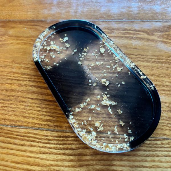 Clear resin tray with gold flakes on wood surface.