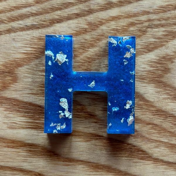 Blue resin letter H with gold flakes on wood.