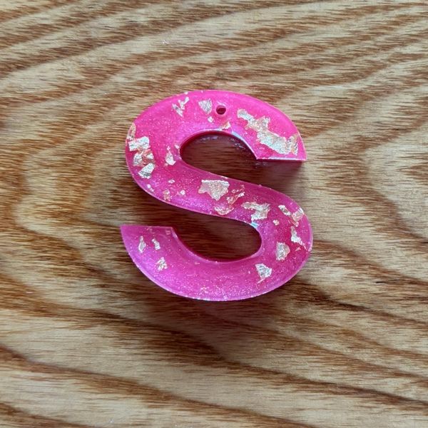 Pink resin letter S with gold flakes on wood.