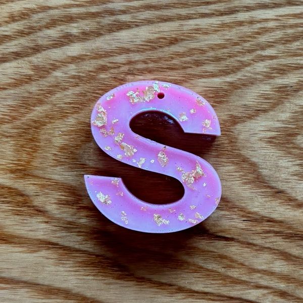 Pink letter 'S' with gold flakes on wood.