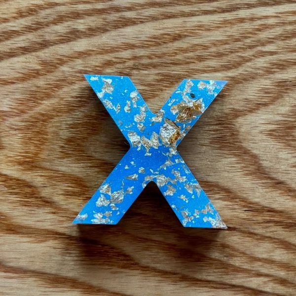 Blue letter 'X' with silver flakes on wood.