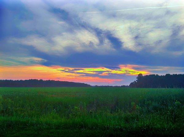 Sunset over a green field with dramatic clouds.