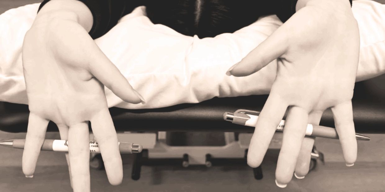Close-up of hands with pens balanced between fingers, person lying face down.