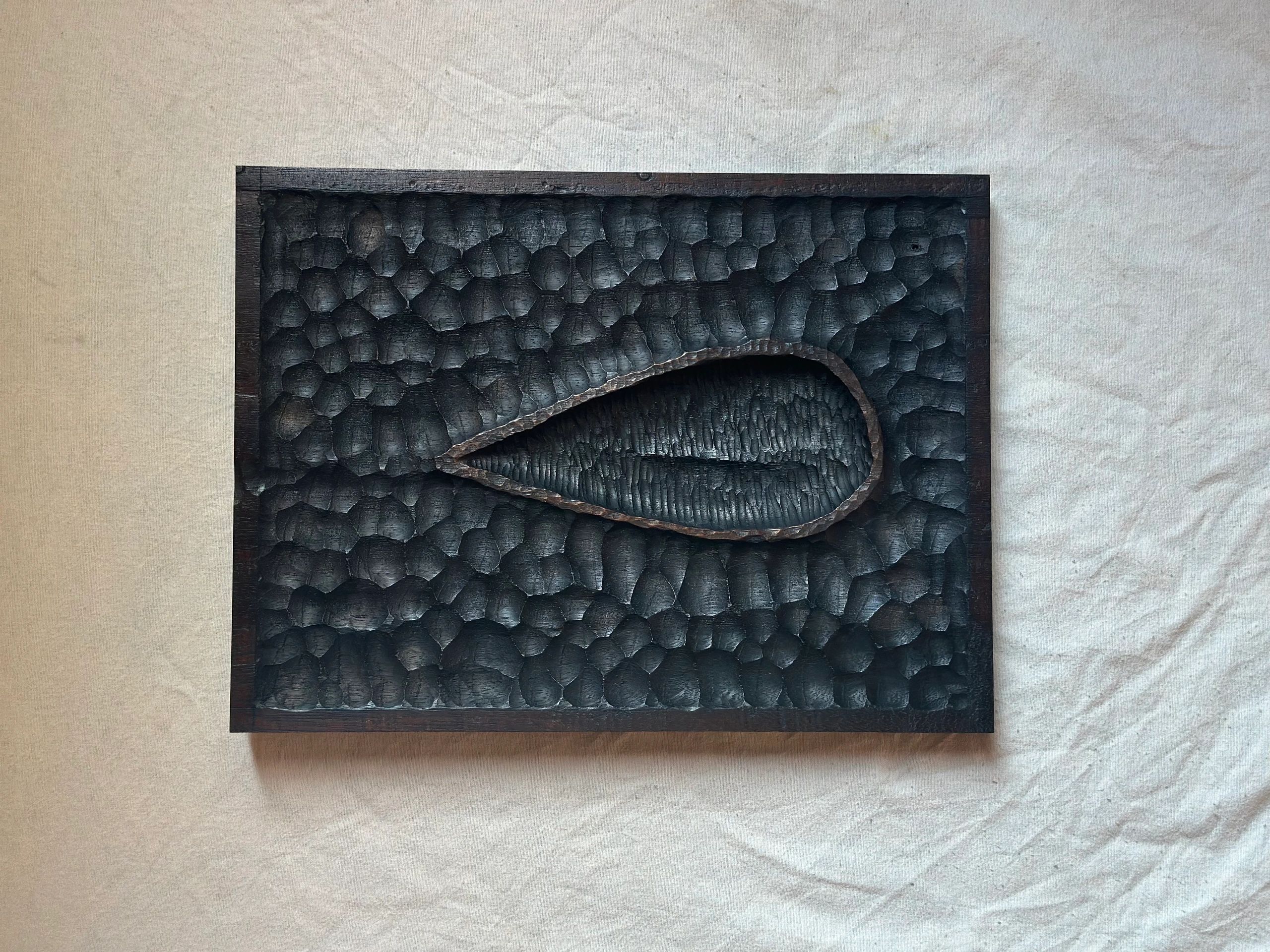 Charred wooden artwork with textured patterns and a teardrop shape in the center.