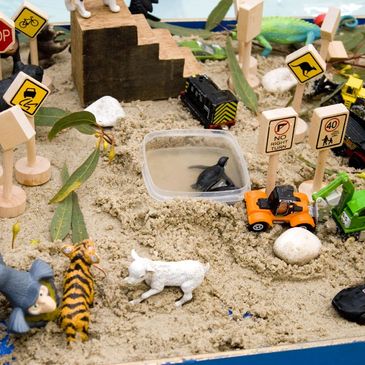 A miniature sandy scene with toy animals, cars, and road signs.