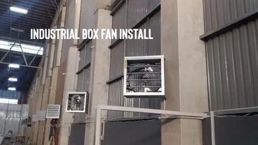 Industrial box fans installed on a large warehouse wall.