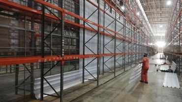 Worker installs metal sheets along warehouse shelves.