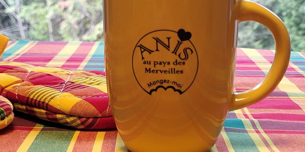 Tasse jaune avec inscription "ANIS au pays des Merveilles" sur une table colorée.
