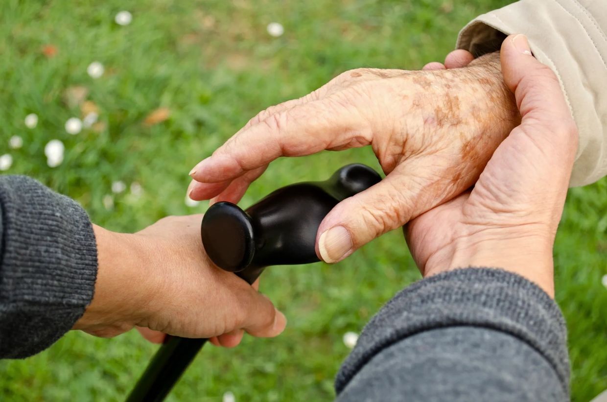 Young hands helping elderly hand to grasp cane