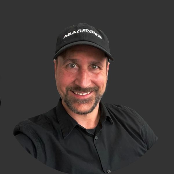 Smiling man in a black shirt and cap on a dark background.