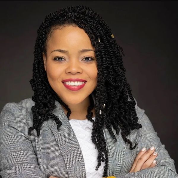 Confident woman with curly hair smiles warmly in professional attire.