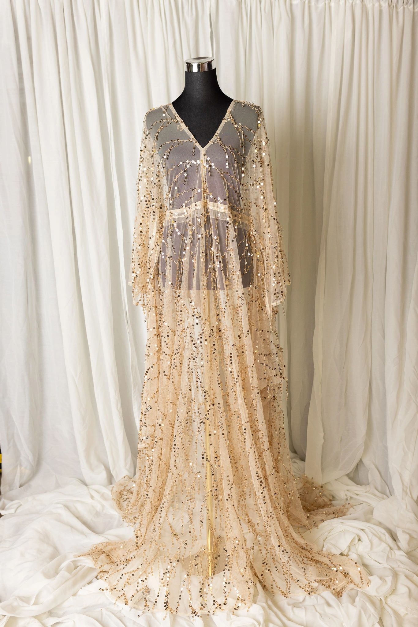 Elegant sheer gown with gold sequins on a mannequin.
