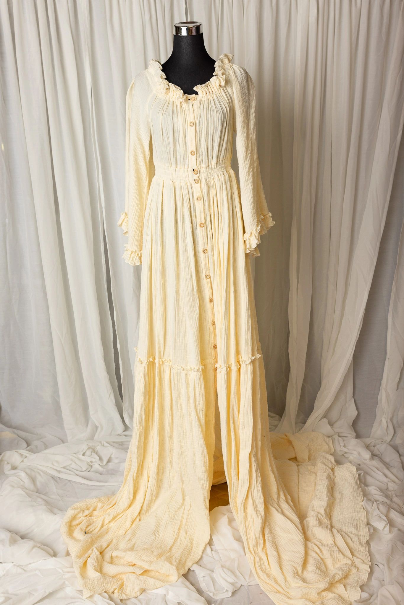 Long cream-colored dress with buttons and ruffles on a mannequin.
