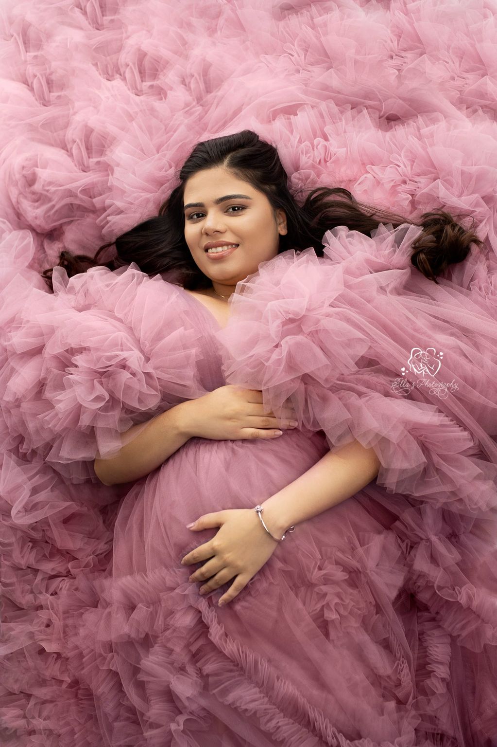 Pregnant woman smiling, wrapped in pink tulle fabric.