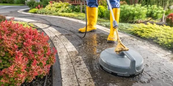 Person in yellow boots pressure washing a garden pathway.