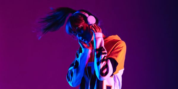 Young woman enjoying music with headphones in vibrant purple lighting.