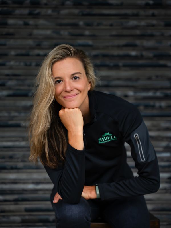 Woman smiling with hand under chin, wearing a black SWELL jacket.