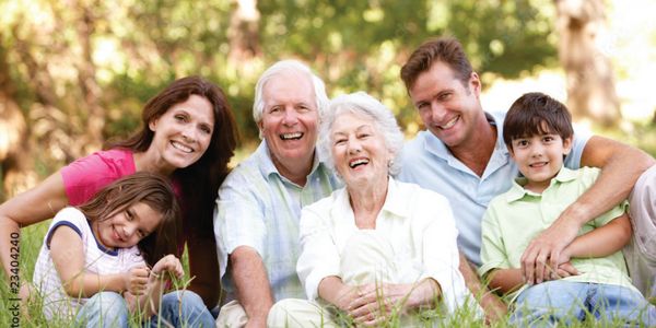 A happy multigenerational family sitting together outdoors, smiling at the camera.