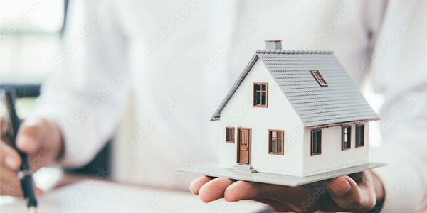 Person holding a small house model while signing documents.