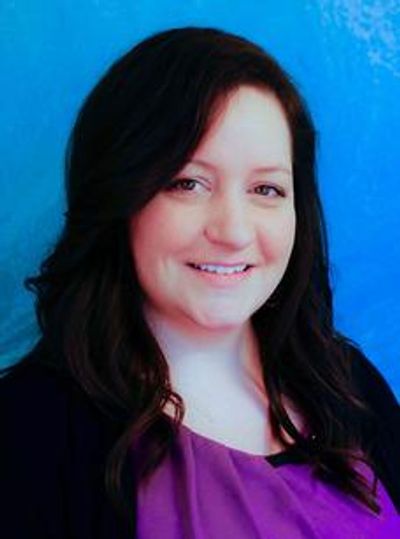Smiling woman with dark hair and purple top against blue background.