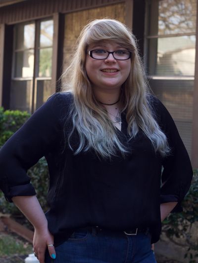 Smiling young woman in glasses stands outdoors.