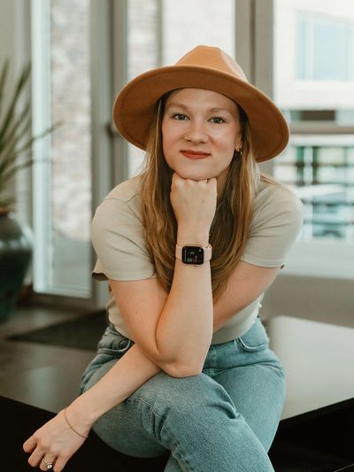 Young woman in a hat sitting and posing with a smile.