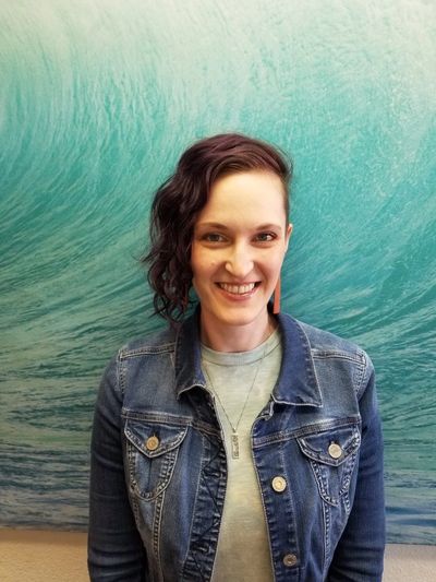 Smiling woman with curly hair wearing a denim jacket.