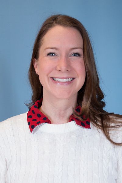 Smiling woman with brown hair and blue eyes in a white sweater.