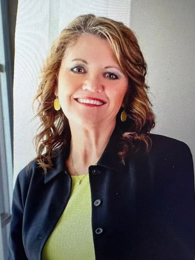 Smiling woman with wavy hair wearing a black jacket and yellow top.