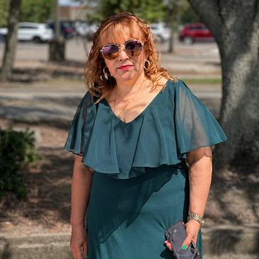 Woman in teal dress and sunglasses standing outdoors on a sunny day.